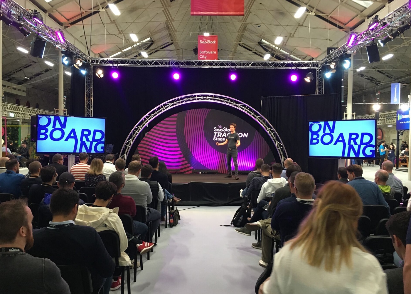 photo of James giving a talk to a crowd, there are two screens on stage that both say ONBOARDING