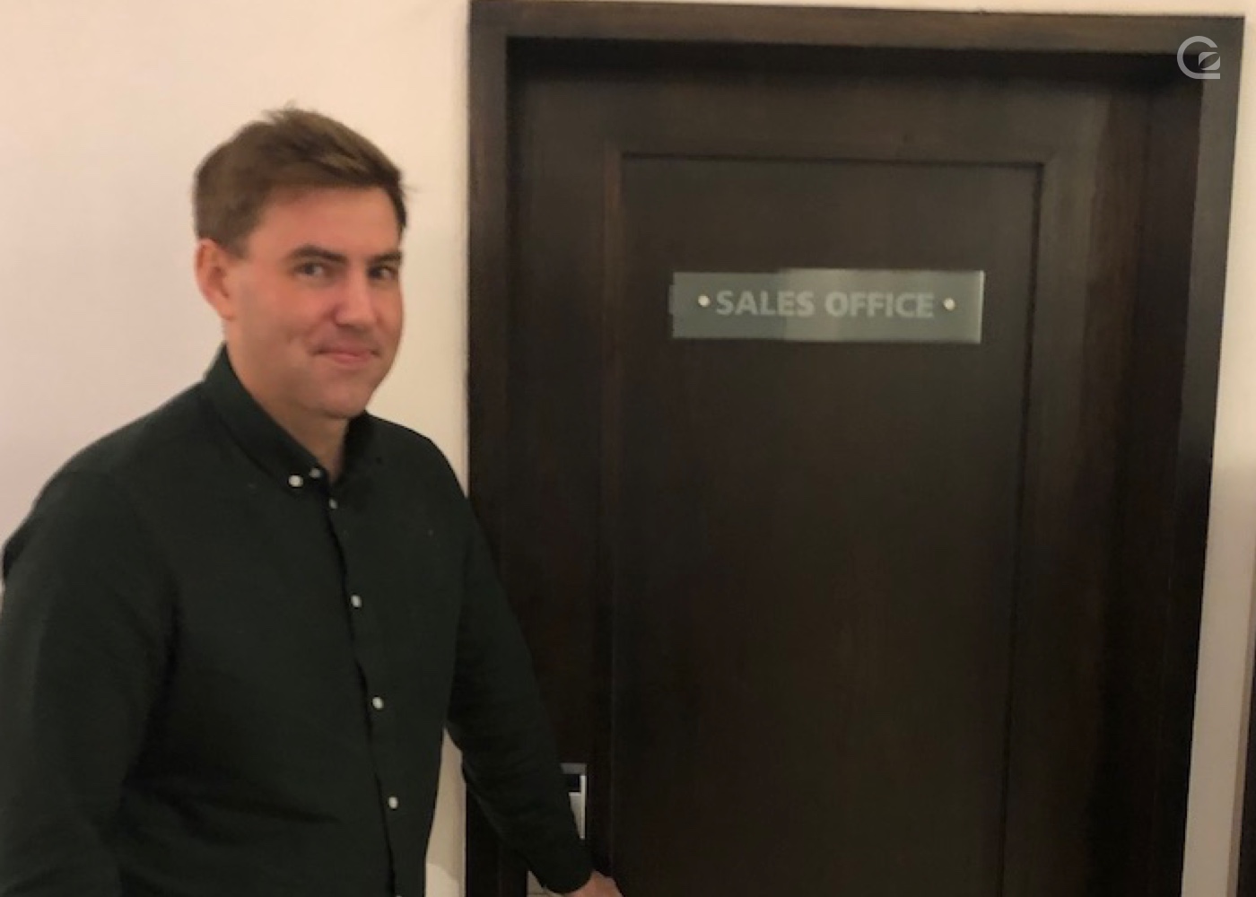 photo of Russell standing next to a door that has a sign on it reading 